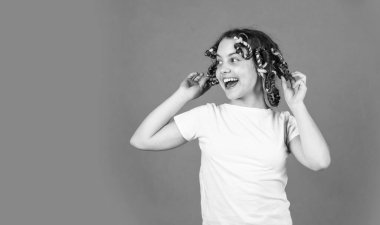 Moda ipuçları. Kıvırcık saçlı, turuncu saçlı küçük bir kız. Sevimli çocuk saçı. Gençlik hobileri. Kafasında bigudileri olan kızı gülüyor. Kuaför salonu. Kadın güzellik rutini