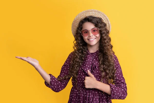 Дівчина посміхається в солом'яному капелюсі і сонцезахисних окулярах з довгим брюнеткою кучеряве волосся на жовтому фоні — стокове фото