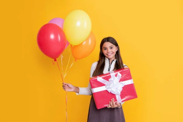 Smiling child with party colorful balloons and present box on yellow background — стоковое фото