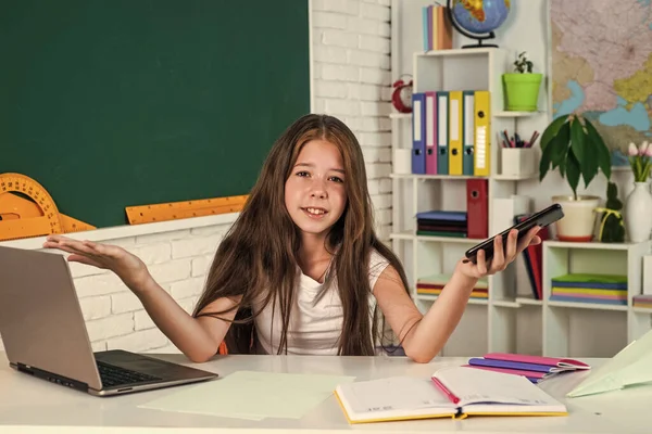 Glad liten flicka hålla mobiltelefon på laptop i skolan lektion, formell utbildning — Stockfoto