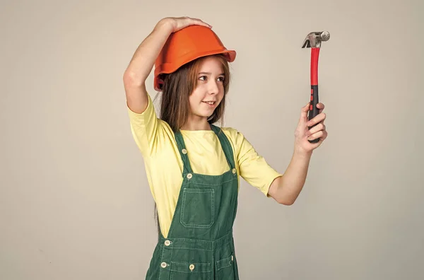 Tonåring flicka arbetare i skyddshjälm och uniform på grå bakgrund användning hammare, arbetare — Stockfoto