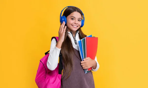 Sonrisa infantil en auriculares con mochila escolar con cuaderno de trabajo sobre fondo amarillo — Foto de Stock