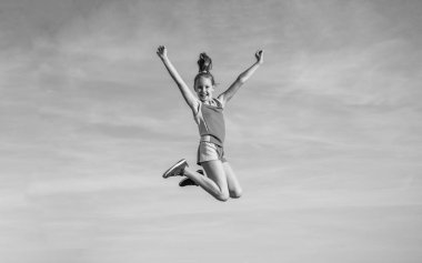 esniyor ve ısınıyor. çocukluk mutluluğu. Sağlık ve zindelik. Jimnastik. Özgürlük duygusu. Mutlu genç kız gökyüzü arka planında zıplıyor. Çocuğun esnek bir vücudu var. Spor kıyafetli çocuk eğitimi