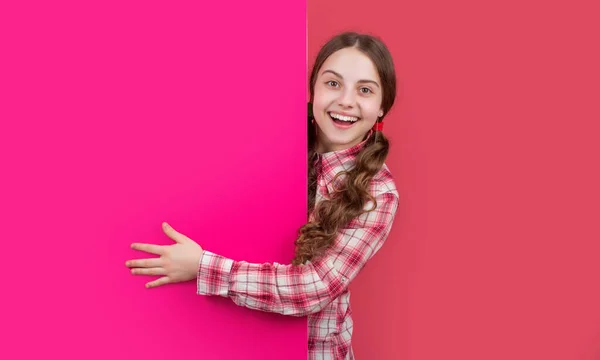 Menina maravilhada feliz atrás de papel rosa em branco com espaço de cópia para propaganda — Fotografia de Stock