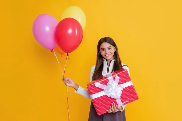 Glad child with party helium balloons and present box on yellow background — стоковое фото