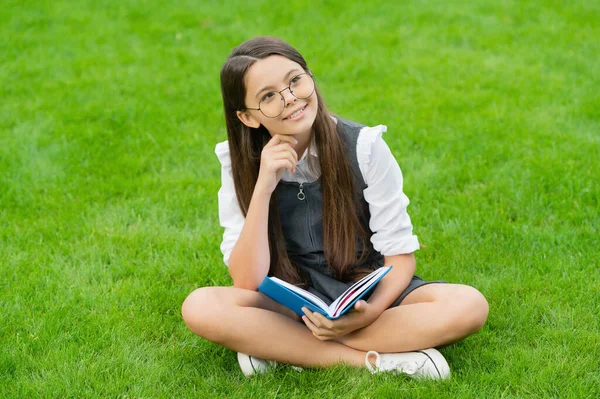 Méditer enfant dans des lunettes livre de lecture assis sur l'herbe verte — Photo