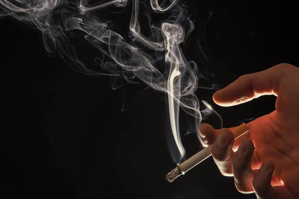 Mężczyzna ręka trzymać palenie papieros z dym strumień ciemne tło przestrzeń kopia, zły nawyk — Zdjęcie stockowe