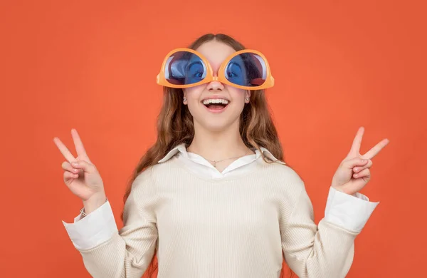 Glückliches Kind mit großer lustiger Sonnenbrille auf dem Kopf macht V-Sings Geste braunen Hintergrund, Frieden — Stockfoto