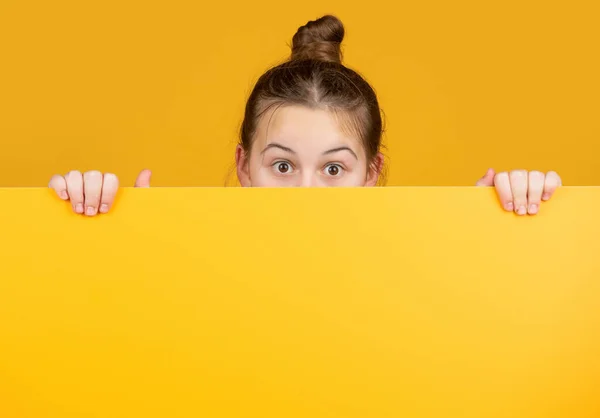 Dítě skrývající se za prázdným žlutým papírem s kopírovacím prostorem pro reklamu — Stock fotografie