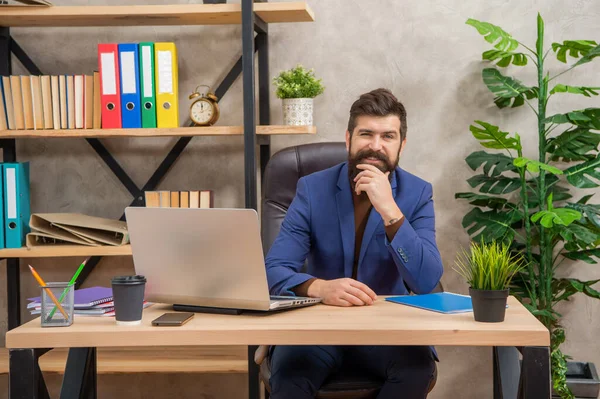 Cheerful brutal ceo in businesslike suit with pc at the office, online — стоковое фото