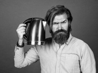 Bıyıklı ve sakallı acımasız bir adam. Elektrikli ev aleti. Sakallı adam kırmızı elektrikli su ısıtıcısı kullanıyor. Erkek ev idaresi konsepti. Sıcak suya ihtiyacım var. Adam çay ya da kahve içecek.
