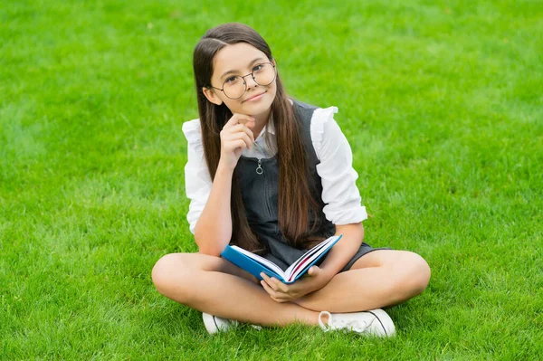 Veselé dítě v brýlích čtení knihy sedí na zelené trávě — Stock fotografie