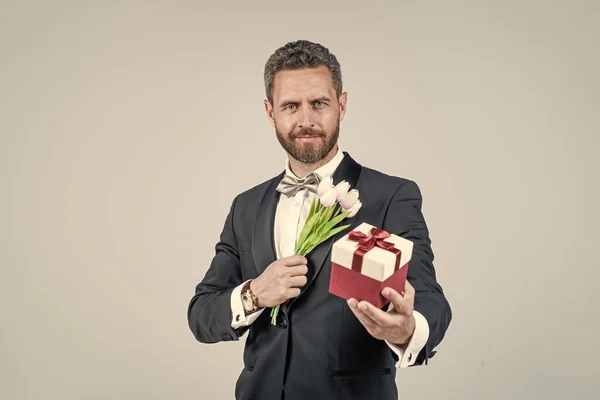 Bonito smoking homem segurar caixa de presente e tulipa flores, aniversário — Fotografia de Stock