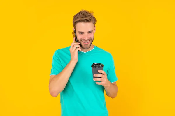 Glad orakad ung man prata på telefon med kaffekopp på gul bakgrund, konversation — Stockfoto