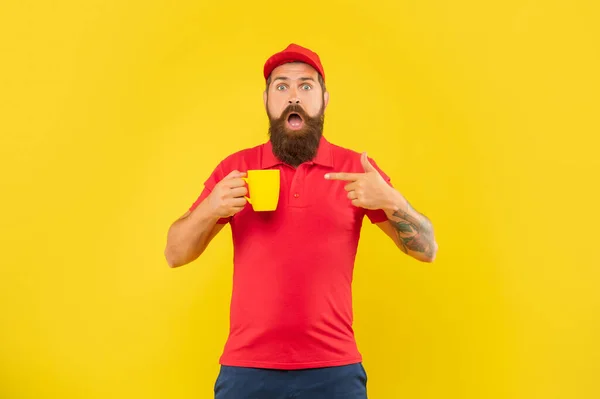 Uomo barbuto scioccato in berretto rosso casual e maglietta che punta il dito verso lo sfondo giallo tazza, tè — Foto Stock