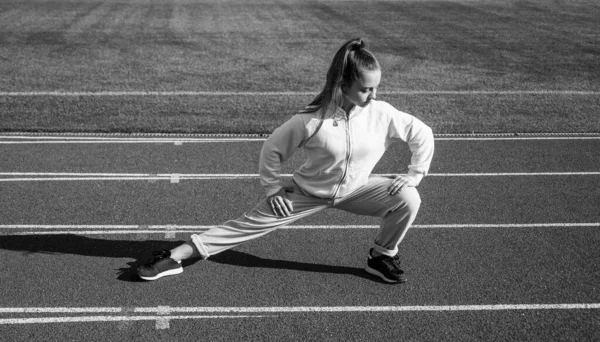 Menina adolescente aquecendo no estádio. miúdo de fato desportivo a esticar-se. criança fazer exercício em pista de corrida. infância saudável. treino ao ar livre ao ar livre. Corredor confiante. corpo flexível — Fotografia de Stock