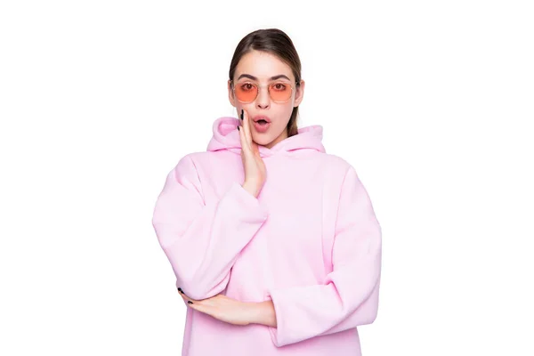 Meglepett nő alkalmi rózsaszín kapucnis pulcsiban és szemüvegben kiabálás wow holding hand at open mouth — Stock Fotó
