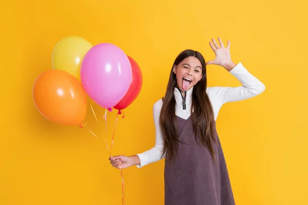 Cheerful child with party helium balloons on yellow background — стоковое фото