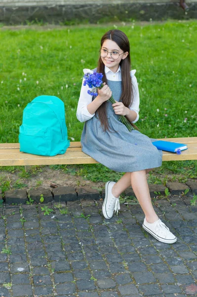 Šťastná dívka v brýlích relaxovat na školní lavici s květinami a batohem. ženský den — Stock fotografie