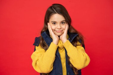 Kış kıyafetleri içinde kızıl arka planda kıvırcık saçlı, gülümseyen genç kız.