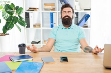 Calm man meditate keeping mudra listening to relaxing music in headphones at office desk, meditation