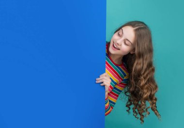 happy curious child behind blank blue paper with copy space for advertisement