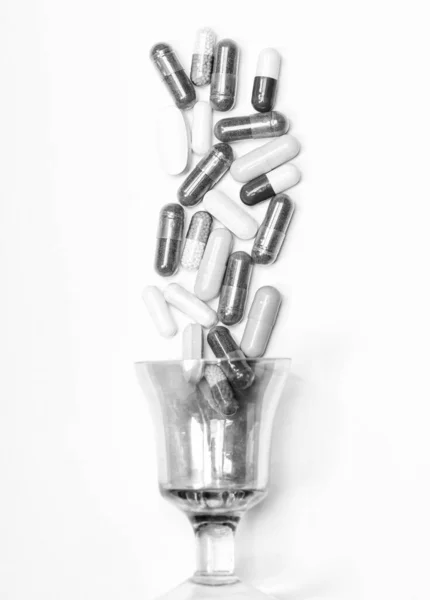 Φάρμακα και φάρμακα. Πολύχρωμα καπάκια χύνονται πάνω από γυαλί. Φάρμακα που απομονώνονται σε λευκό — Φωτογραφία Αρχείου