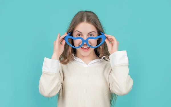 Happy girl child smiling in big funny heart-shaped glasses blue background — Stockfoto