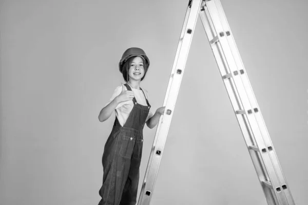 明るいですティーン女の子で作業制服とヘルメット上のはしごを表示親指アップ,建物 — ストック写真