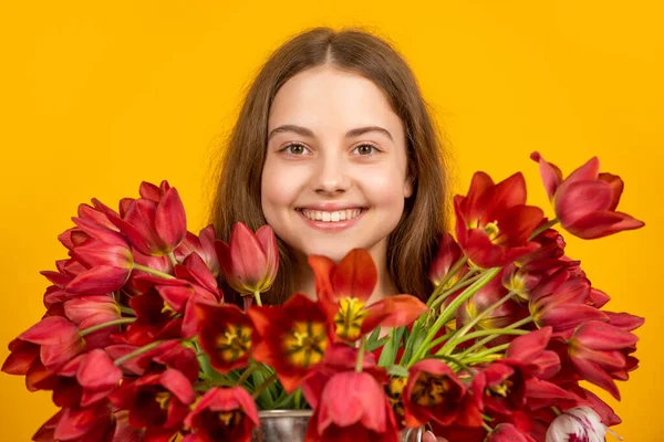 Positive girl hold spring tulip flowers on yellow background — Stock fotografie