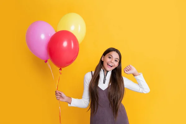 Positive child with party helium balloons on yellow background — стоковое фото