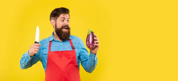 Glad kille i förkläde tittar på aubergine hålla kniv för matlagning gul bakgrund kopia utrymme, kock — Stockfoto
