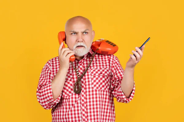 Hombre mayor concentrado con teléfono retro y teléfono inteligente moderno sobre fondo amarillo — Foto de Stock