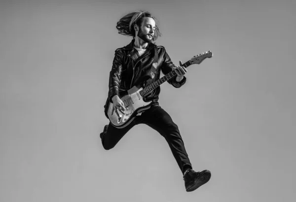 Érzelmi szakállas rockzenész elektromos gitározik bőrdzsekiben és ugrásban, gitáros — Stock Fotó