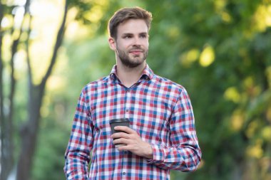 positive young man in checkered shirt with coffee cup