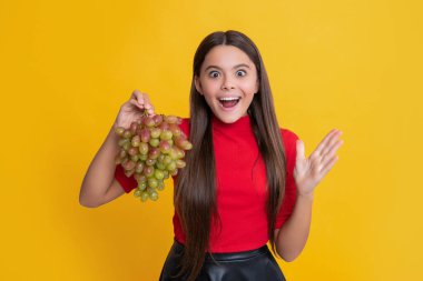 Şaşırmış çocuk sarı arka planda taze üzüm tutuyor.