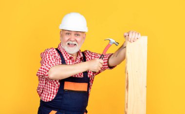 cheerful mature man woodworker in helmet on yellow background