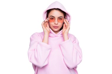 Young fashion woman pouting lips adjusting pink glasses in casual hoodie isolated on white