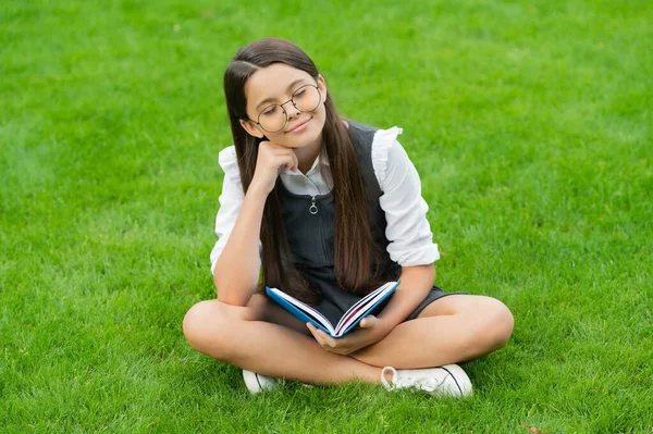 Dreamy child in glasses reading book sitting on green grass — Stok fotoğraf