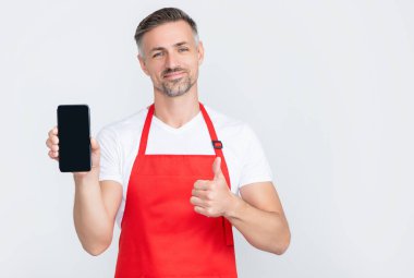 Önlüklü neşeli olgun bir adam akıllı telefona fotokopi alanı sunuyor. başparmak yukarı