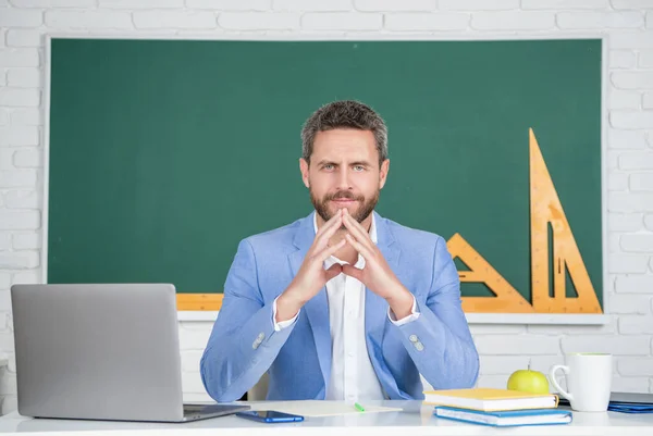 Positive school teacher in classroom with laptop at blackboard — Stockfoto