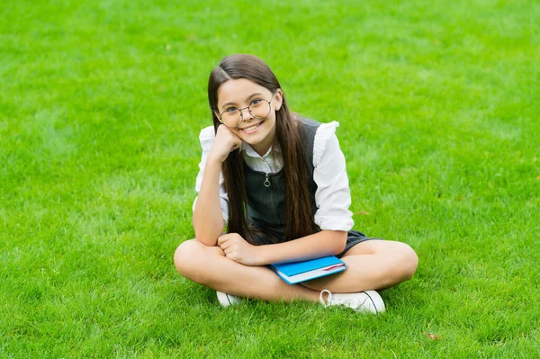 Glad child in glasses sitting on green grass with book — Stok fotoğraf