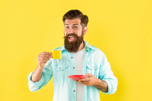 Amazed bearded man drink morning coffee on yellow background, barista — стоковое фото