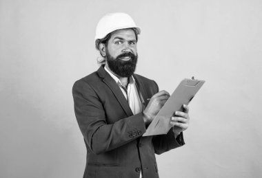 Miğferli ve takım elbiseli ciddi bir ustabaşı kâğıt klasörüne not alıyor.