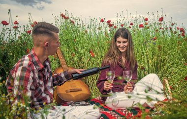 Aşık mutlu çift, akustik gitarlı, müzik serenatıyla gelincik çiçeğinin güzel tarlasında rahatlar.