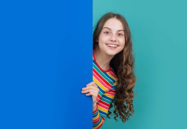 glad girl behind blank blue paper with copy space for advertisement