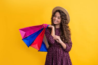 smile child with curly hair hold shopping bags on yellow background