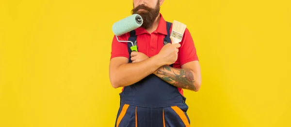 Hombre recortado en ropa de trabajo mantenga rodillo de pintura y cepillo sobre fondo amarillo —  Fotos de Stock