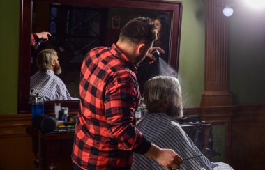 Kişisel tarzını takip ediyor. Usta berber saç stilini ve saç stilini kurutma makinesiyle yapıyor. Berber dükkanı kavramı. Berber dükkanında sakallı genç bir hippi saçını kesiyor. Profesyonel kuaför işi.