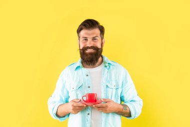 Ciddi sakallı adam sabah kahvesini sarı arka planda içer.